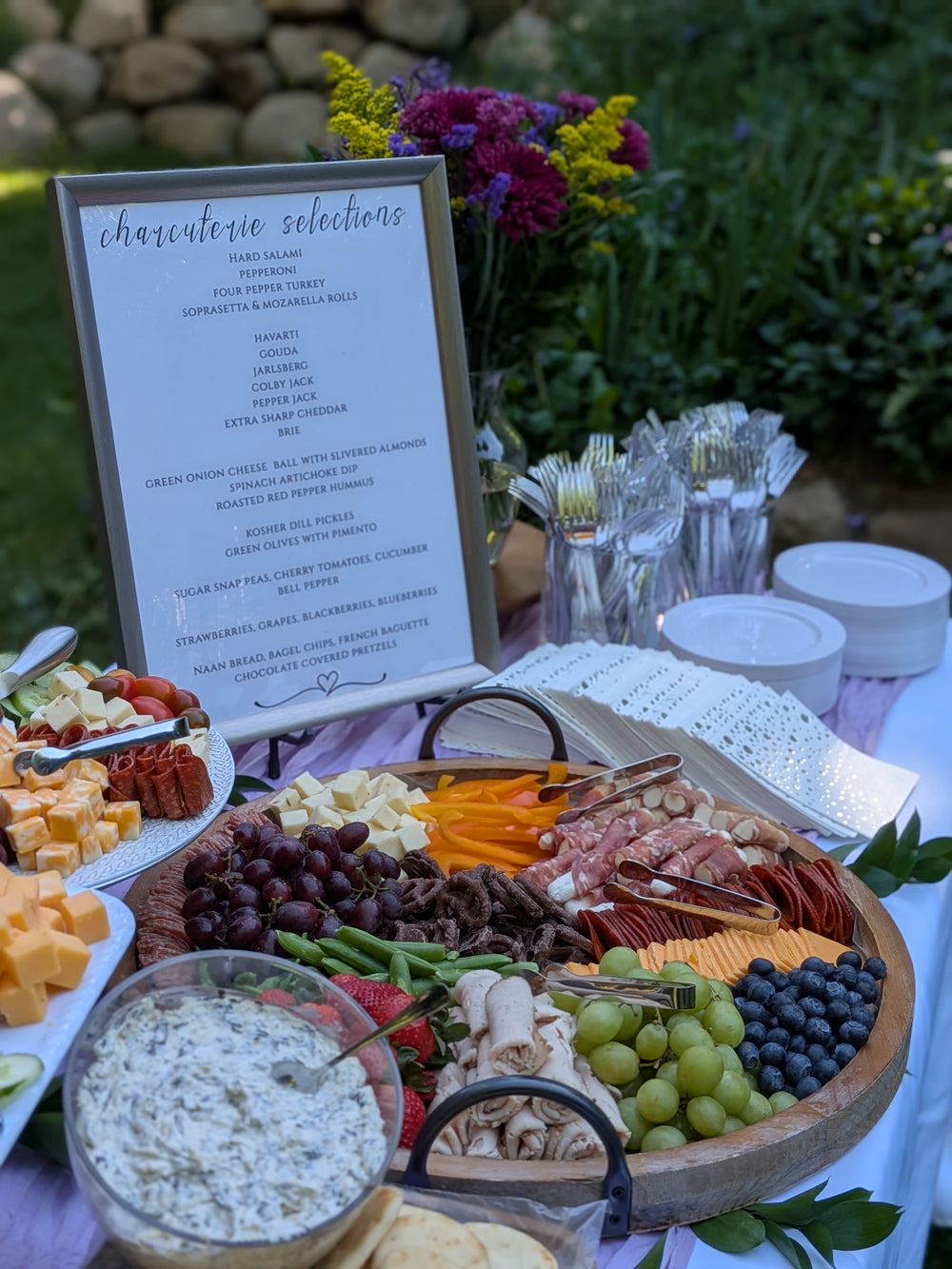Charcuterie boards displayed on a table at an elegant event.  Meats, cheeses, spinach artichoke dip, fresh fruit.  