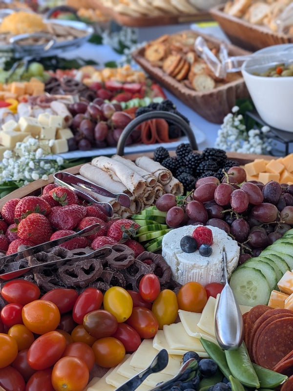Large charcuterie display of multiple charcuterie boards consisting of meats, cheeses, veggies, fruit, breds, chips, and chocolate covered pretzels.  