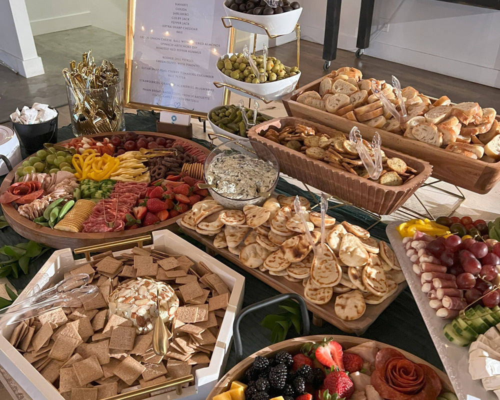 Assorted food platters including fruits, cheeses, and crackers on a table.  Charcuterie boards presented on a table.   