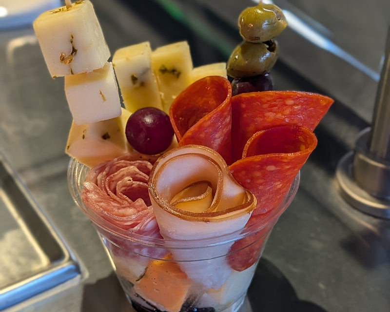 Charcuterie cup with folded meats, cheese and fruit on toothpicks in a clear cup.   