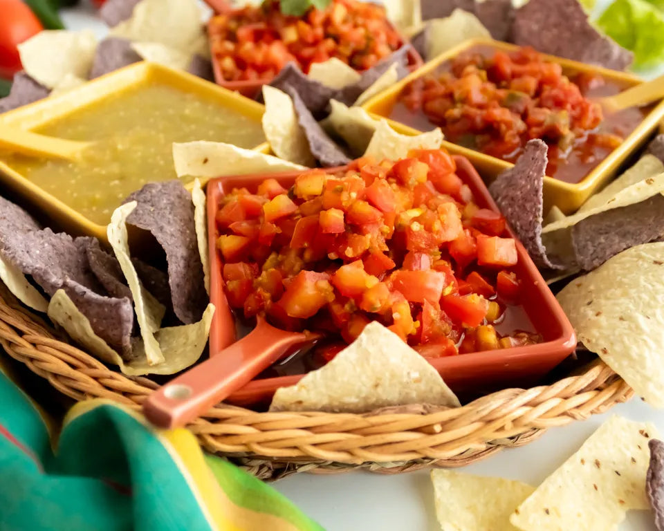 Assorted tortilla chips with salsa in a basket on a white surface