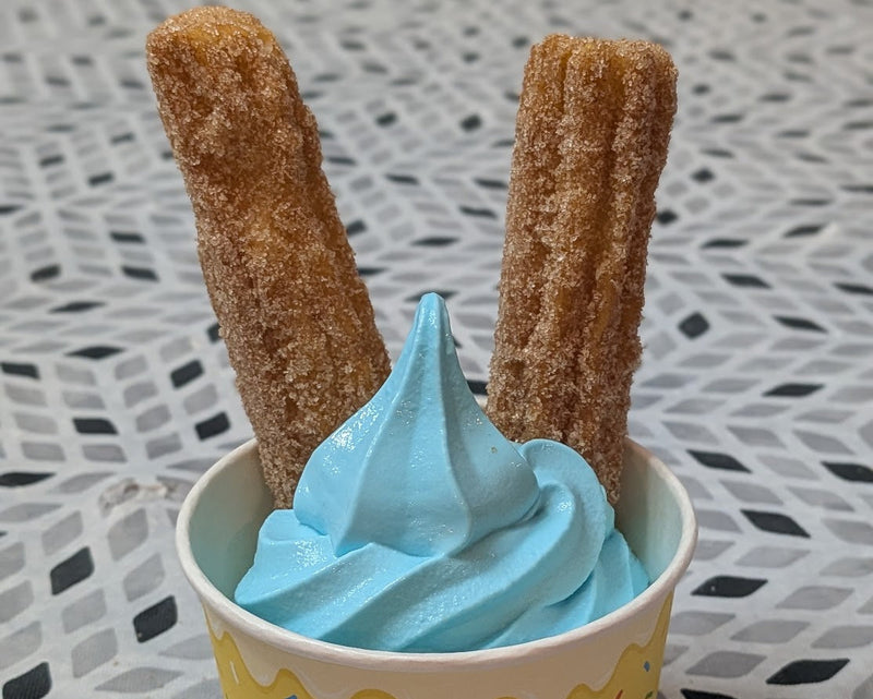 Ice cream bowl with light blue ice cream and two churros placed in the back of the bowl.  