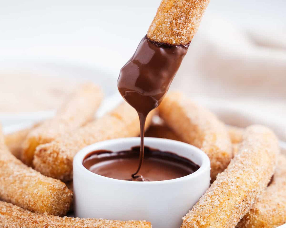 Crispy sugar covered churro being dipped in chocolate sauce in a while bowl.  