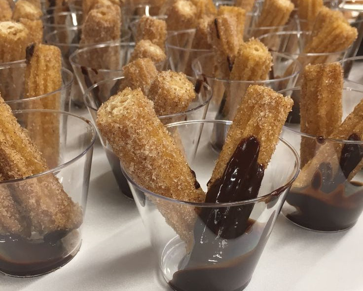 Churros with chocolate dipping sauce in small cups on a white surface.