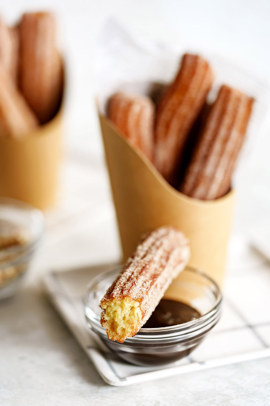 Churros with a side of chocolate dipping sauce on a white surface.