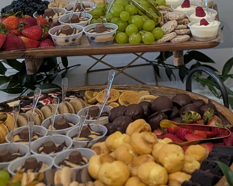 Dessert platter with pastries, fruits, and small containers on a wooden stand.