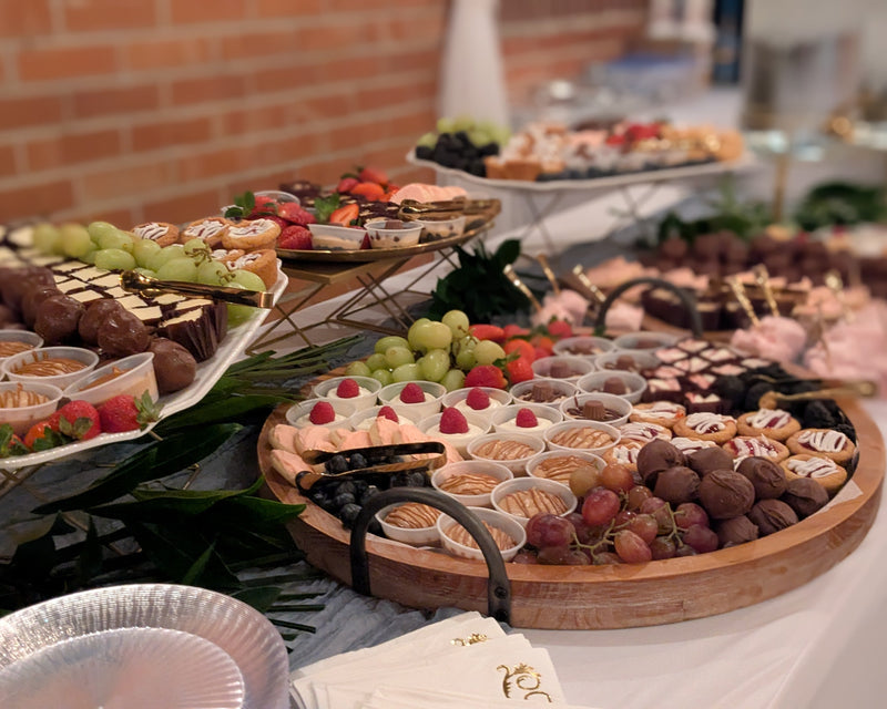 Dessert table with various pastries and fruits on a wooden tray.