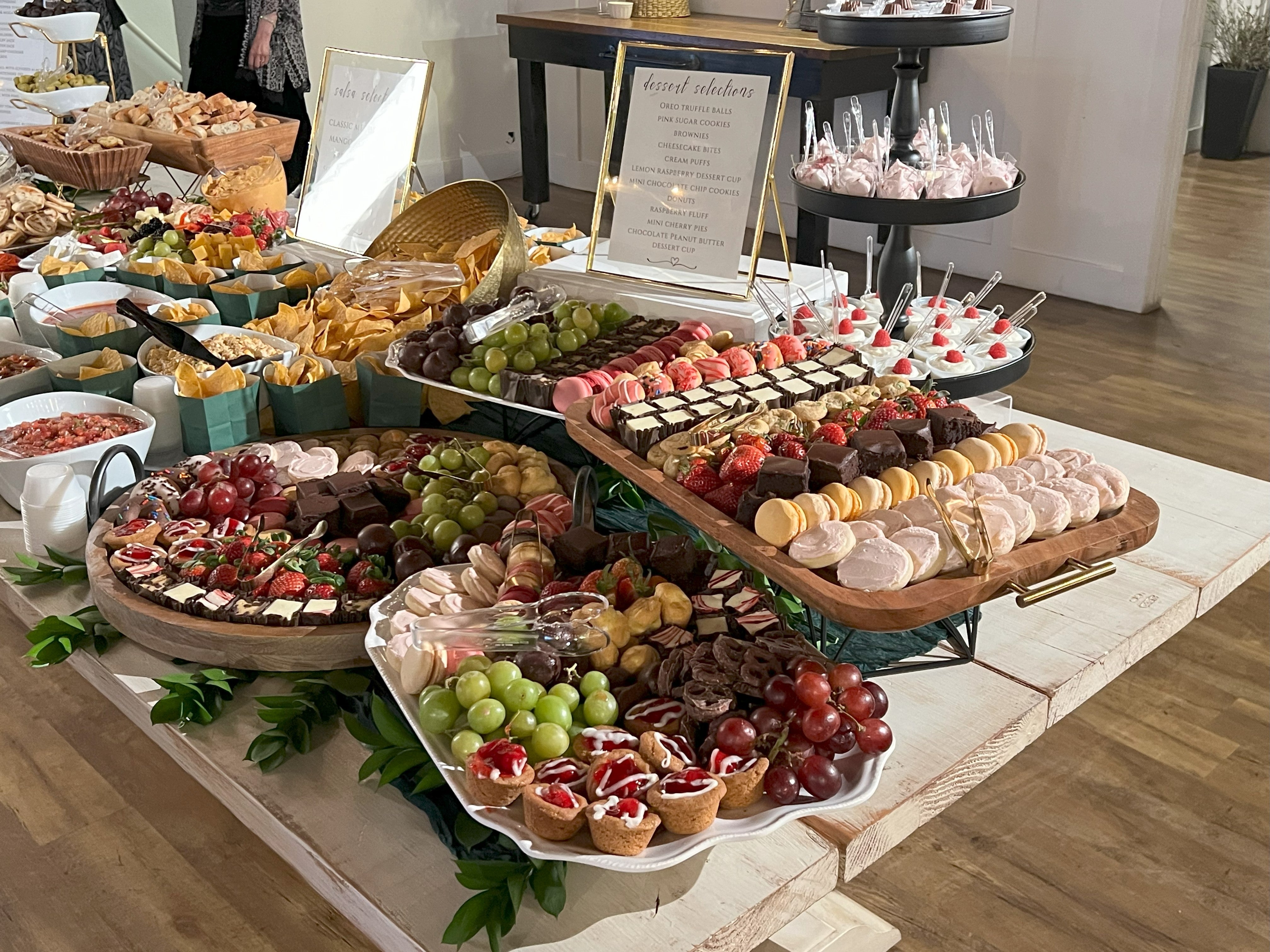Large trays of desserts finely presented in an elegant setting.  Dessert options include fresh cookies, cheesecakes, brownies, dessert cups, raspberry mousse, fresh fruits and macaroons.  