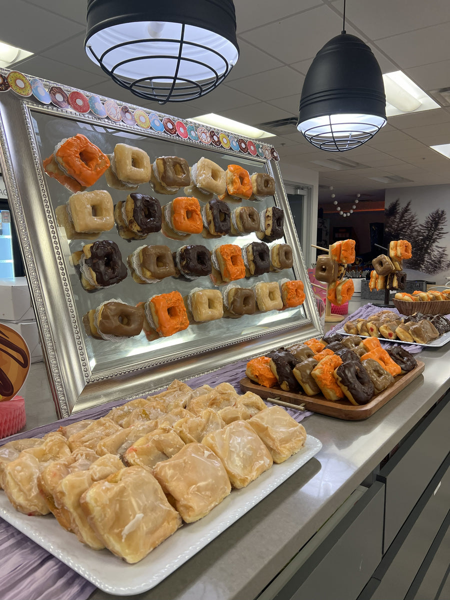 Donuts displayed on a large mirror.  Donuts on stands and platters on a large a countertop.  