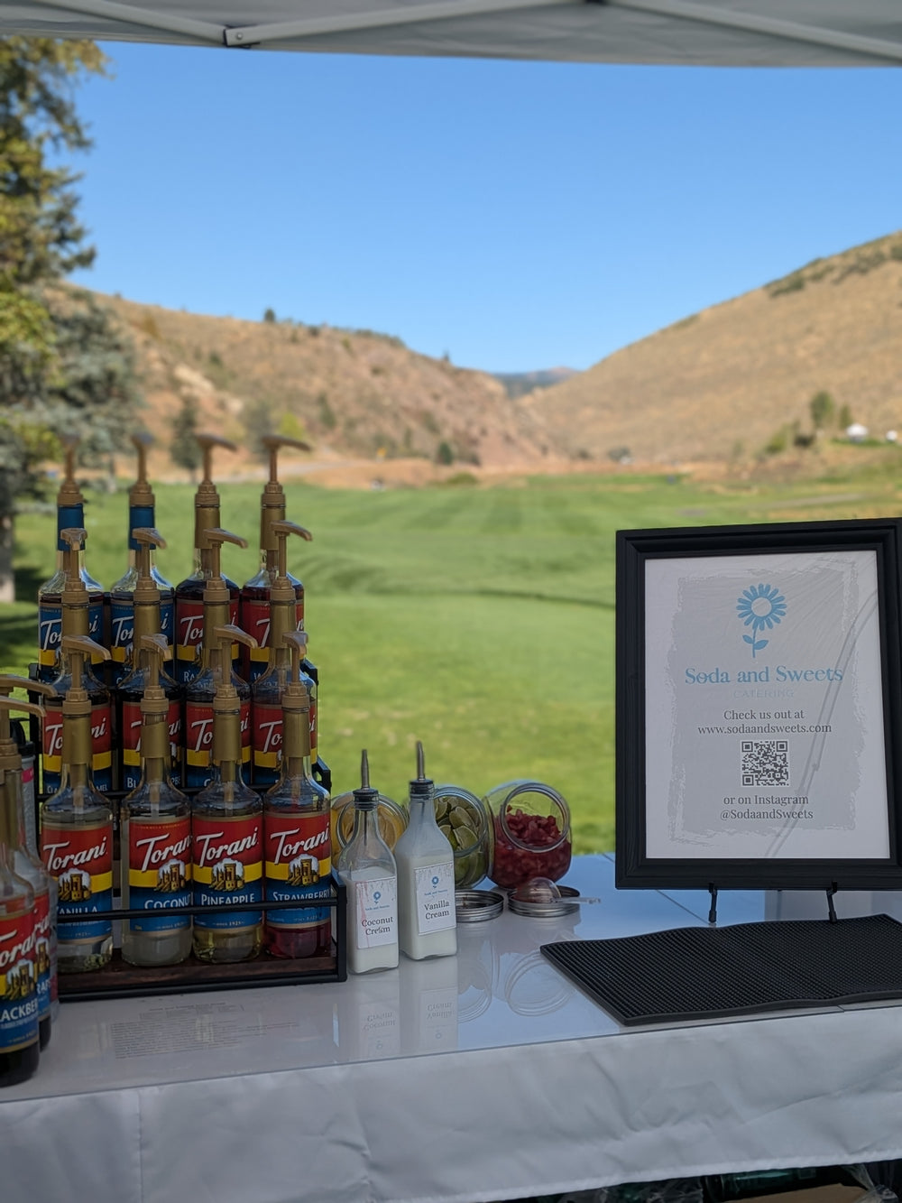 Soda bar with flavored soda mixins on the tee box of a golf course.  Mountains and the golf course fairway are seen in the distance.  