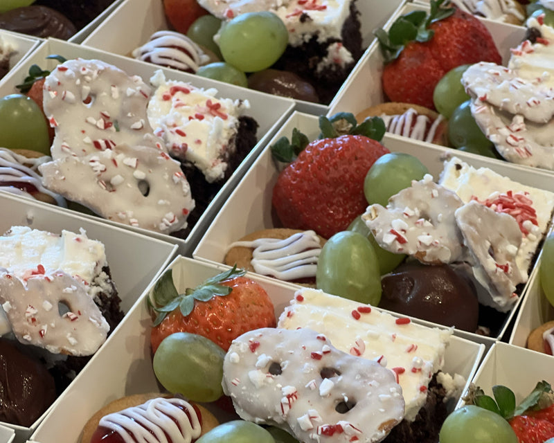 Holiday themed treat boxes with strawberries, green grapes, mini cherry pies, candy cane coated pretzels.  