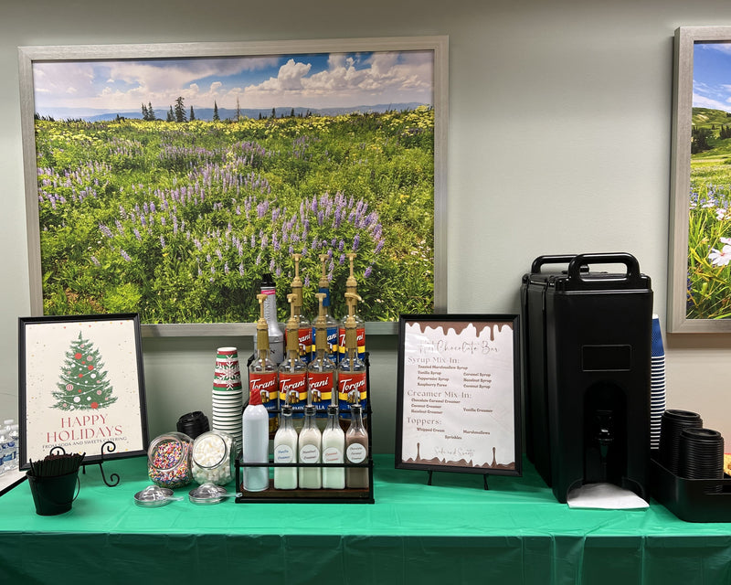 Event setup with hot chocolate, condiments, and a decorative sign on a green tablecloth.