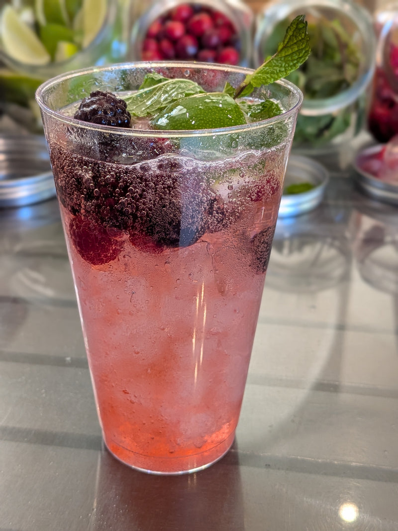 Pink non-alcoholic mocktail with berries and mint in a clear glass on a reflective surface.