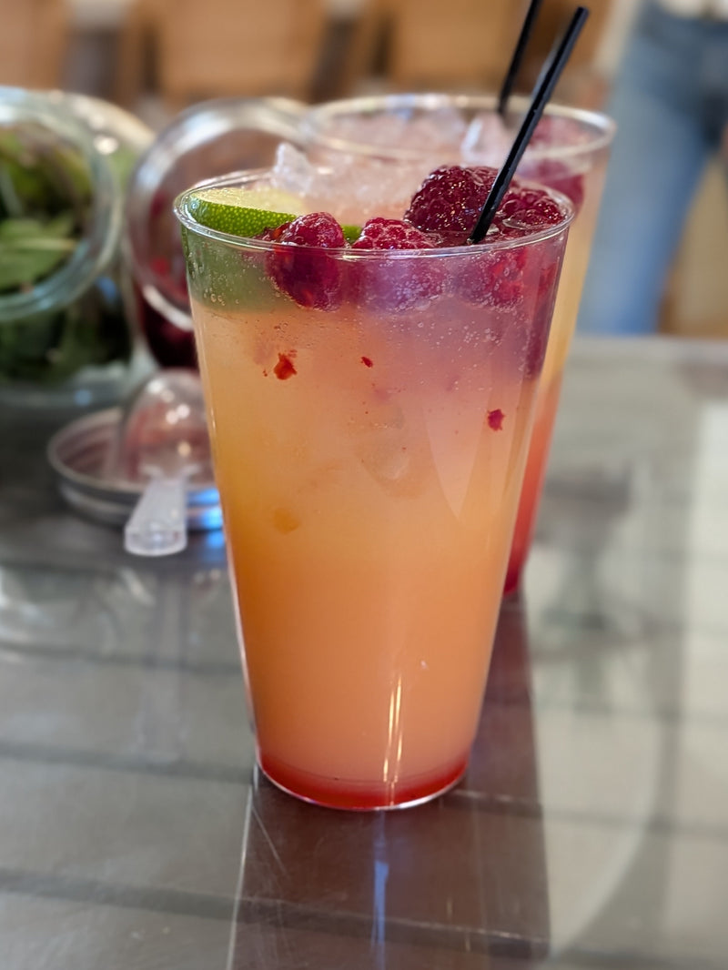 Non-alcoholic mocktail with orange juice, raspberries, and a lime on a trendy countertop.  