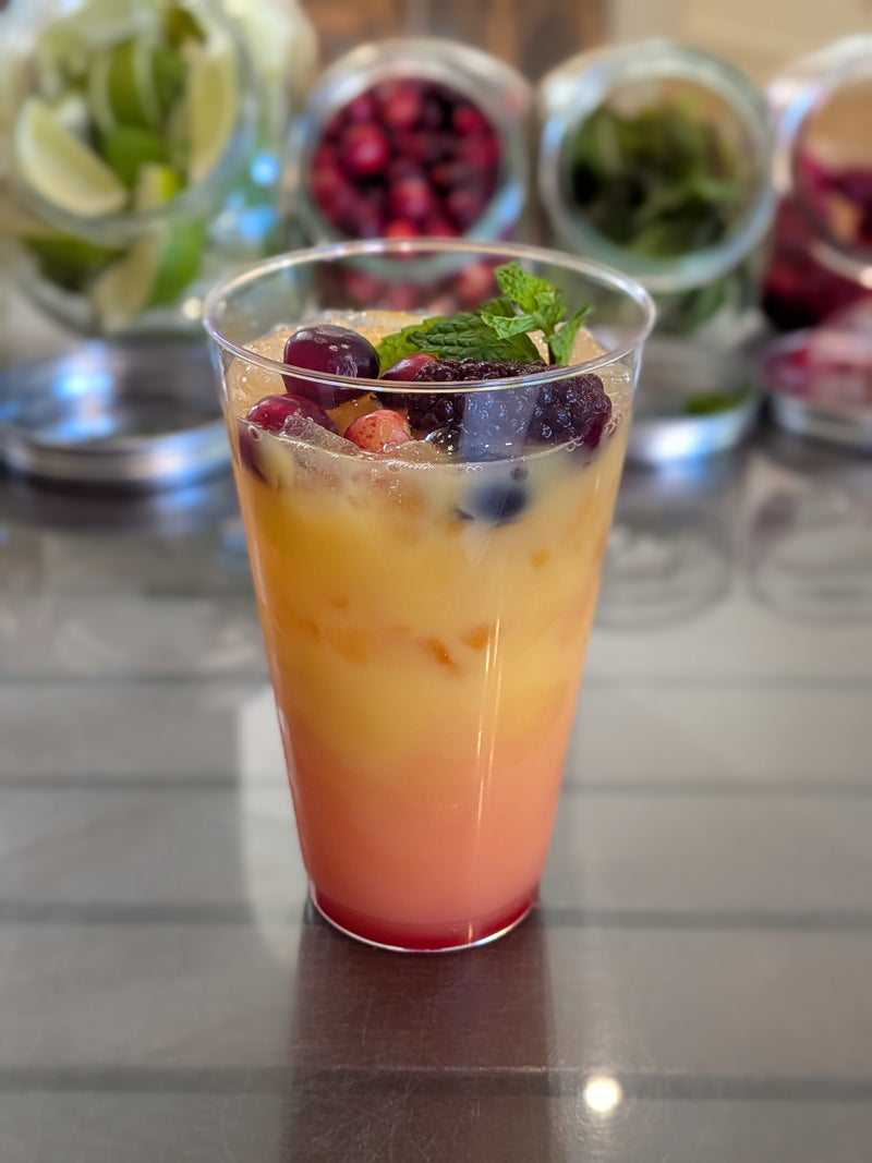 Non-alcoholic mocktail with orange juice, grenadine, grapes, strawberries, and raspberries in a clear cup.  