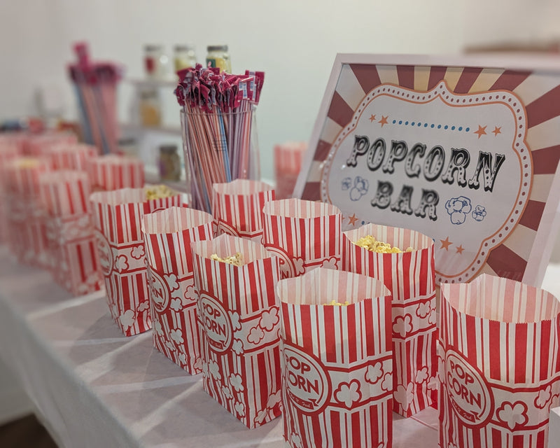 Popcorn bar setup with striped popcorn buckets and a sign in a room.