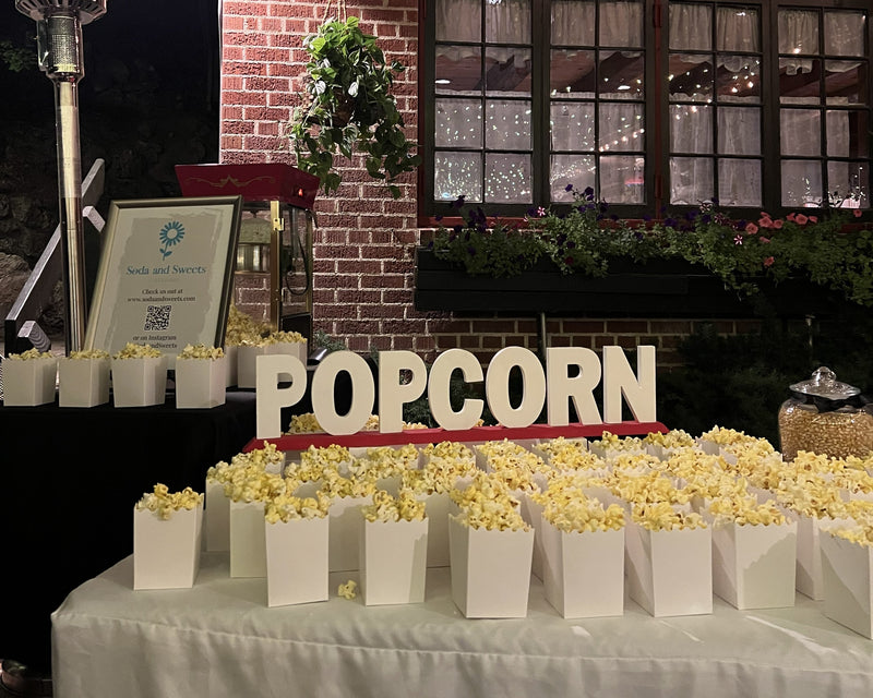 Popcorn table setup with 'POPCORN' sign in front of a brick building at night.