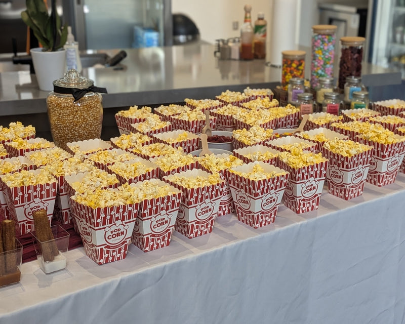 Freshly popped popcorn in boxes on a table,  toppings and flavor salts nearby.  