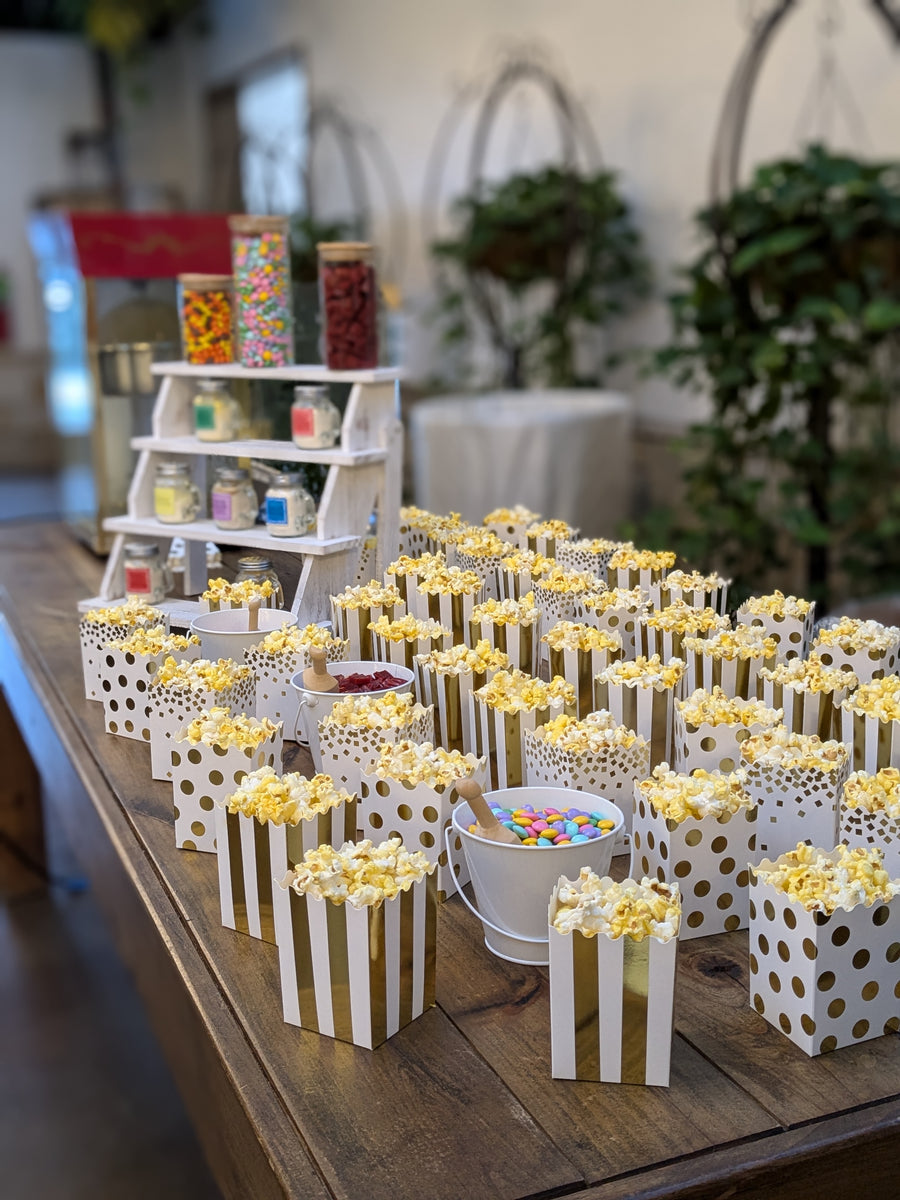 Boxes of popcorn displayed on a large wooden table with flavorings and candy in the background.  