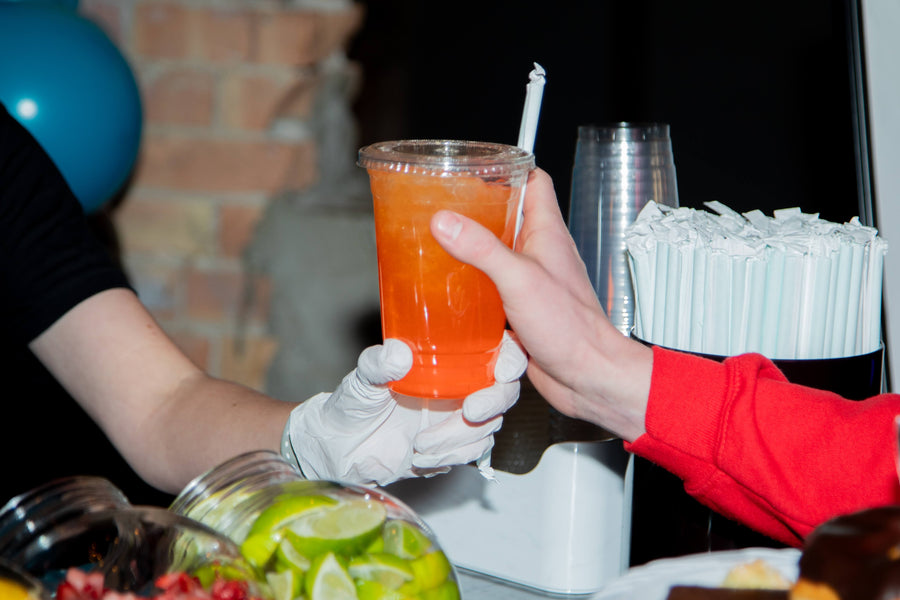 A clear cup with a custom flavored soda with ice in front of a brick wall.  