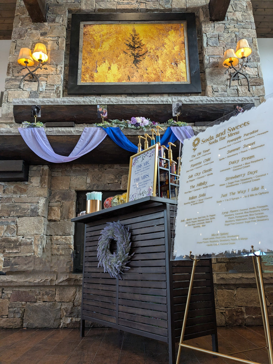 Utah soda bar in front of a majestic fireplace with a large mantle and picture hanging above the fireplace.   The soda bar is configured to service guests flavored sodas.  