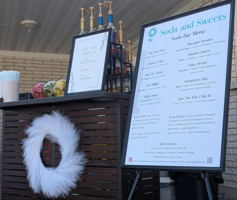 Soda bar.  Outdoor bar setup with flavored soda drink menus, cups, and decorative wreath.