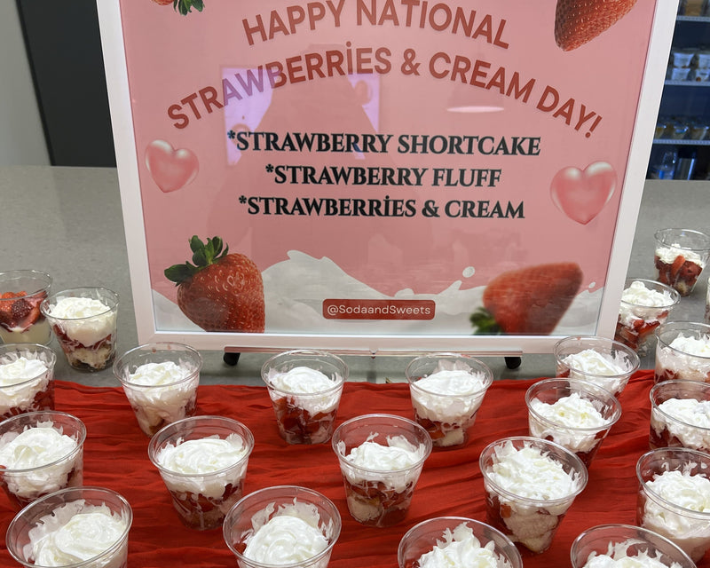 Table with strawberry shortcake and fluff desserts under a 'Happy National Strawberries & Cream Day!' sign.