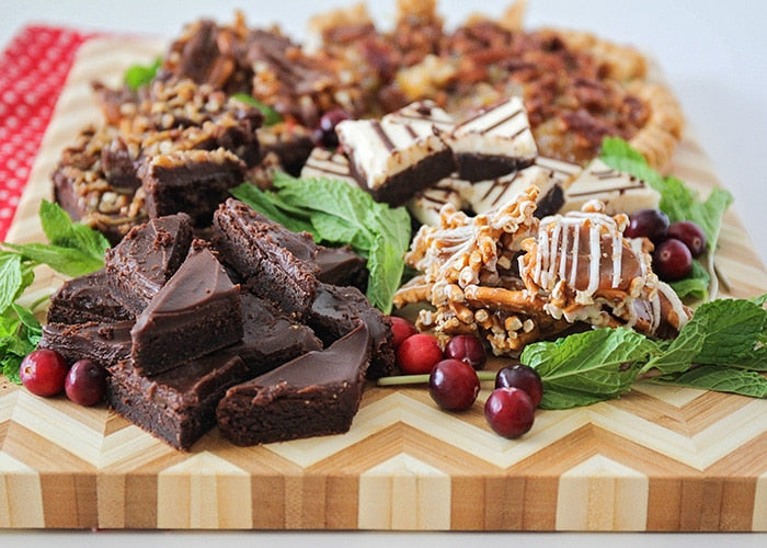 Desserts displayed on a cutting board.  A variety of brownies and fruit.  
