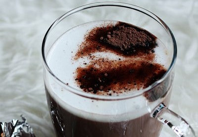 Large cup of warm hot chocolate topped with whipped cream and sprinkled with some fresh cocoa powder.  