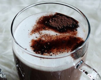 Glass of hot chocolate with a dollop of whipped cream and cocoa powder on a white background