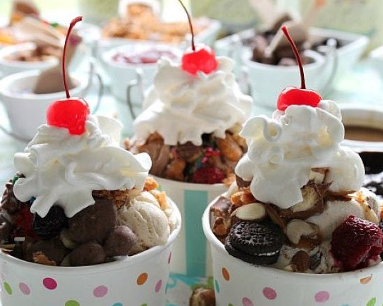 Three bowls of ice cream sundaes with whipped cream, cherries, and various toppings on a blurred background.